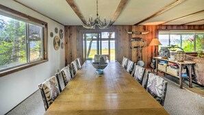 Un comedor con una larga mesa de madera, sillas estampadas, una araña y vistas al exterior.