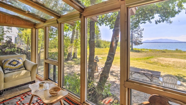 Una habitación luminosa con ventanas amplias, un sofá, una mesita y vistas a un lago y árboles.