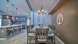 A modern kitchen with stainless steel appliances, a dining area with a large wooden table and chairs, and a decorative tree wall art piece. - Modern El Paso Home w/ Backyard & Fire Pit! (El Paso)
