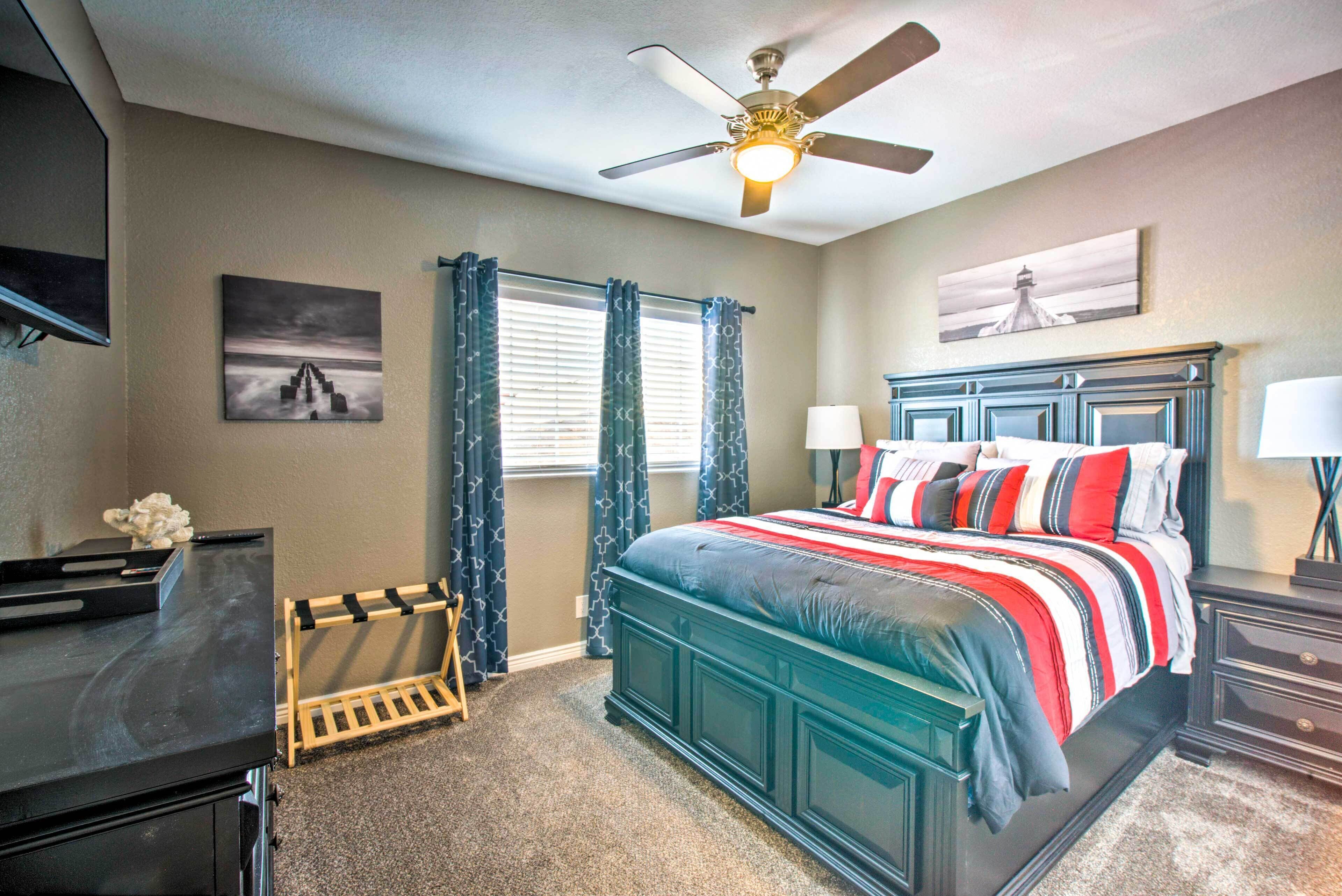 A bedroom with a bed, a ceiling fan, a TV, and a window with curtains.