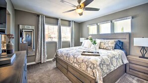 A bedroom with a large bed, a ceiling fan, a dresser, a nightstand, and a window with blinds. - Modern El Paso Home w/ Backyard & Fire Pit! (El Paso)