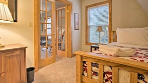 Une chambre avec un lit en bois, une fenêtre avec des stores, une porte donnant sur un balcon et une petite table avec une lampe.