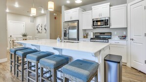 A modern kitchen with white cabinets, stainless steel appliances, and blue bar stools. - Resort Pool & Hot Tub: Modern Condo in St George! (St. George)