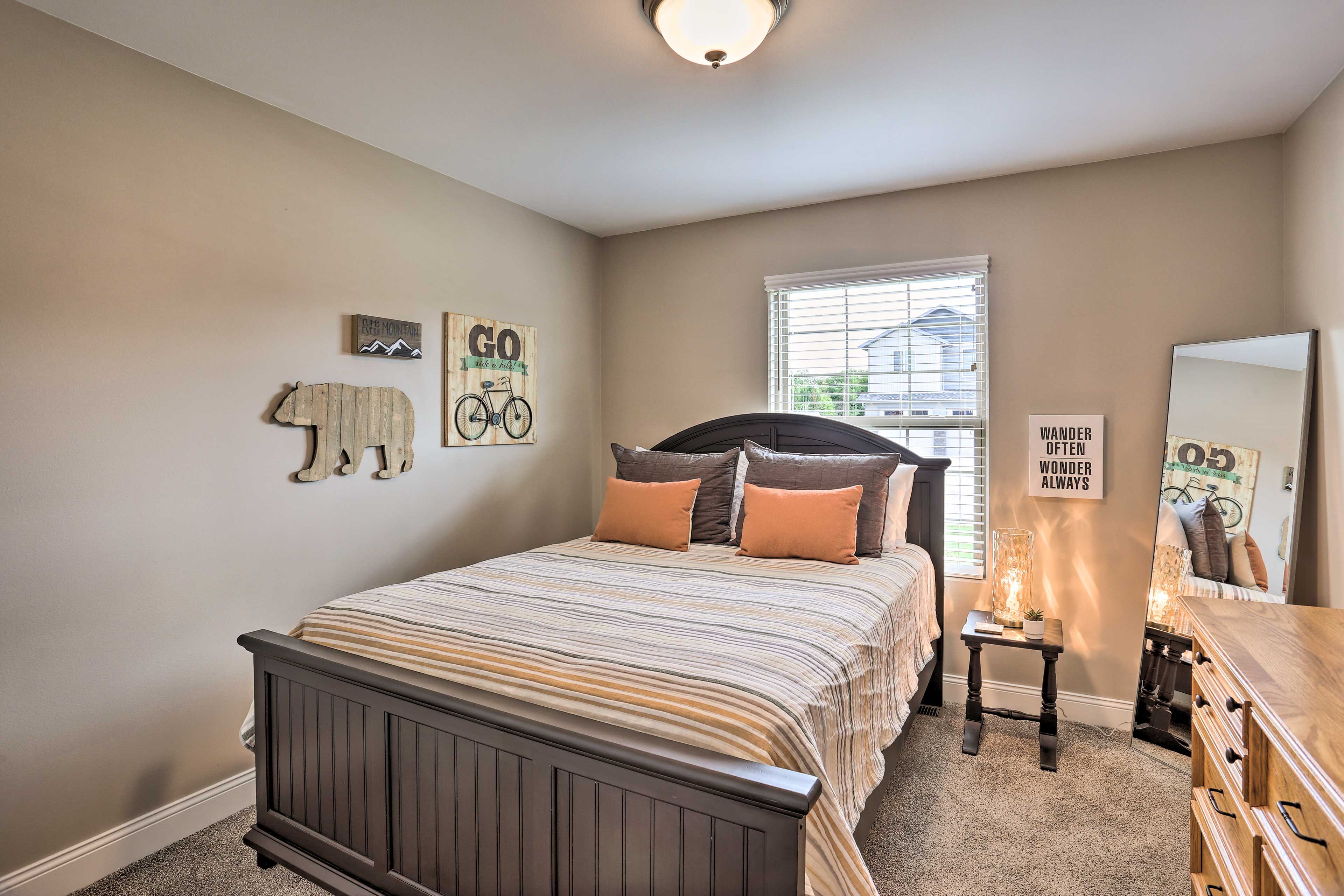 A bedroom with a bed, a dresser, a mirror, and motivational wall art.