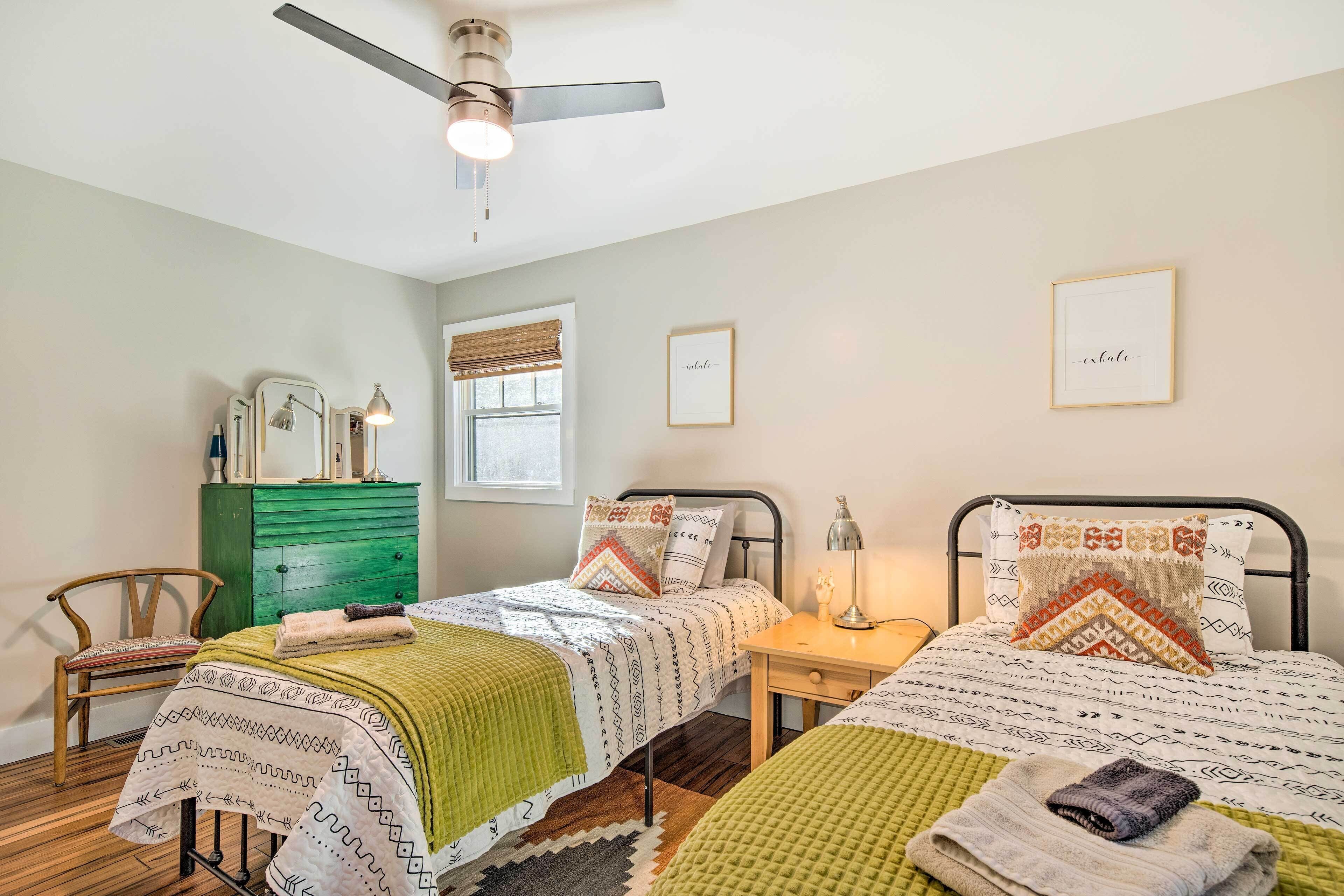 A bedroom with two beds, a dresser, a chair, and a ceiling fan.
