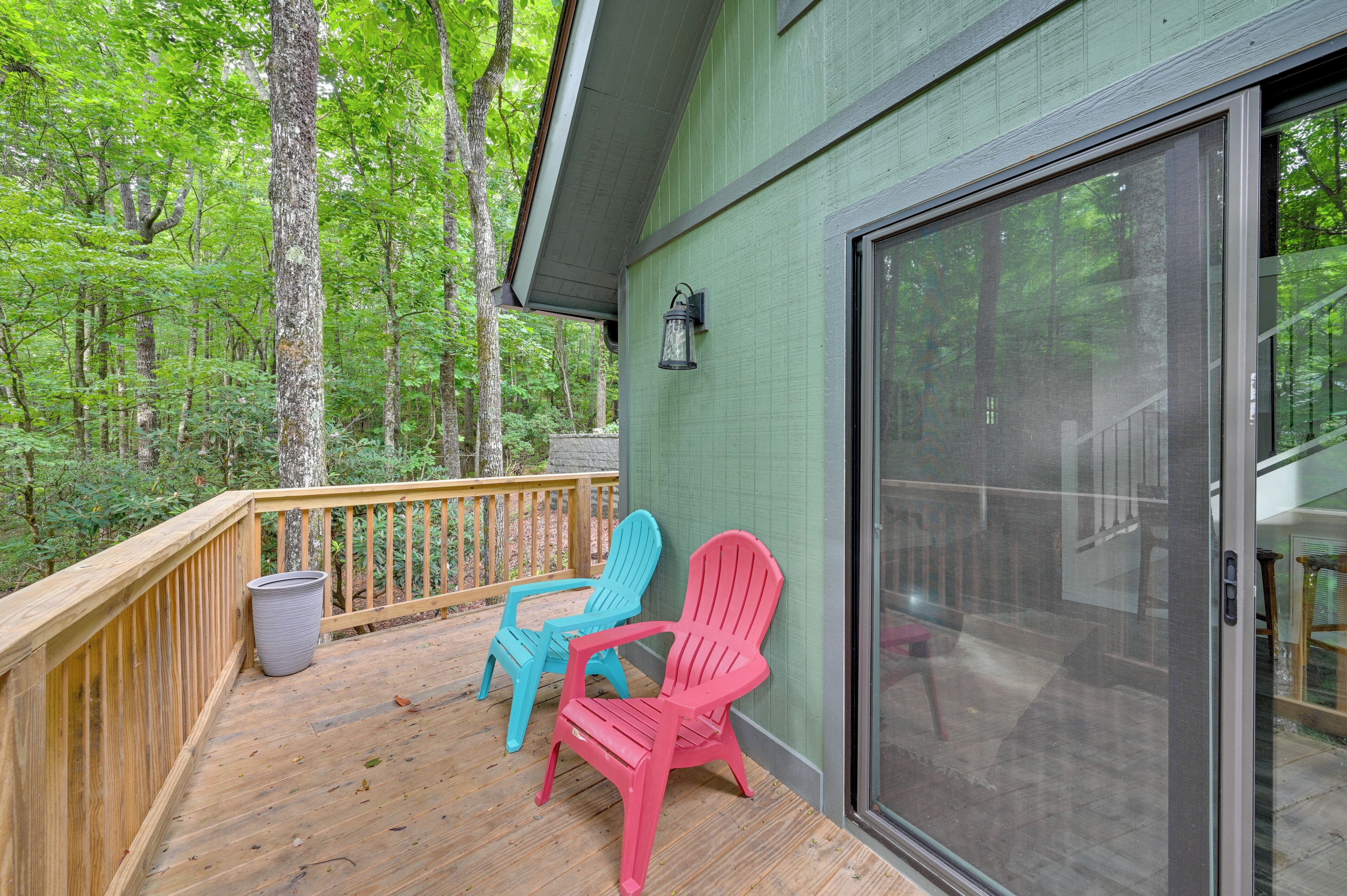 A wooden deck with two Adirondack chairs, a glass door, and a view of a forested area.