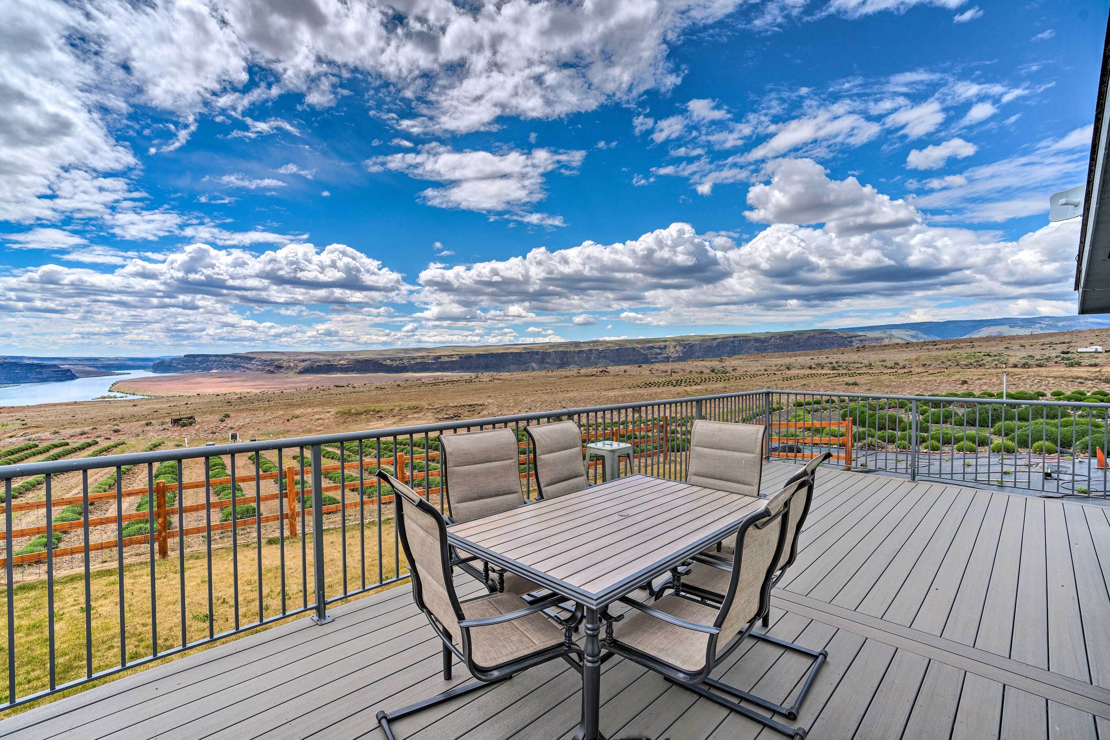 A deck with a table and chairs, overlooking a scenic landscape with a body of water and distant mountains.
