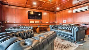 A room with a pool table, leather sofas, and a wooden ceiling.