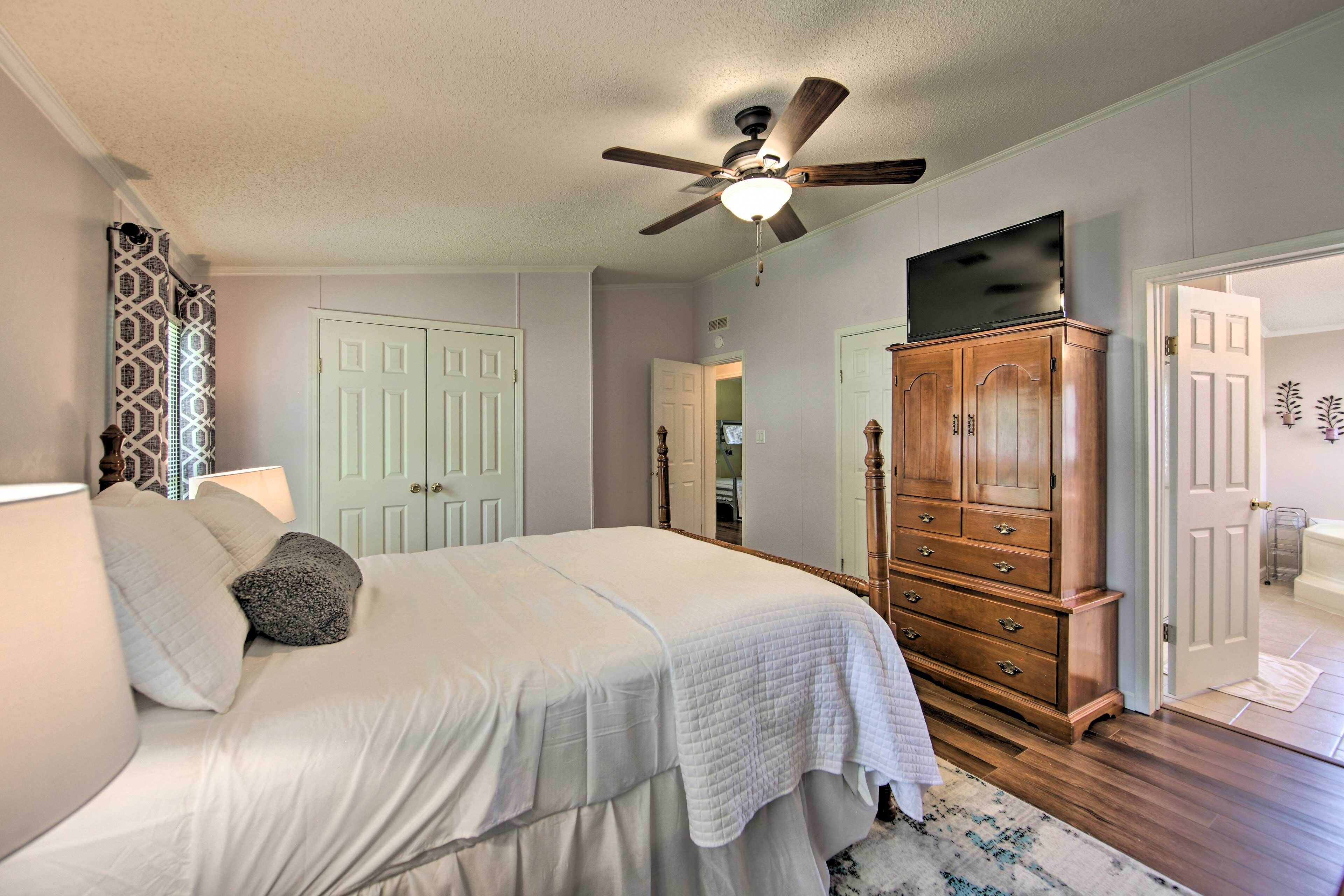 Une chambre à coucher comprenant un lit, un ventilateur de plafond, une commode en bois et une porte donnant sur une autre pièce.