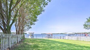 A grassy area with a wooden fence, a gazebo, and a view of a lake with buildings in the background.