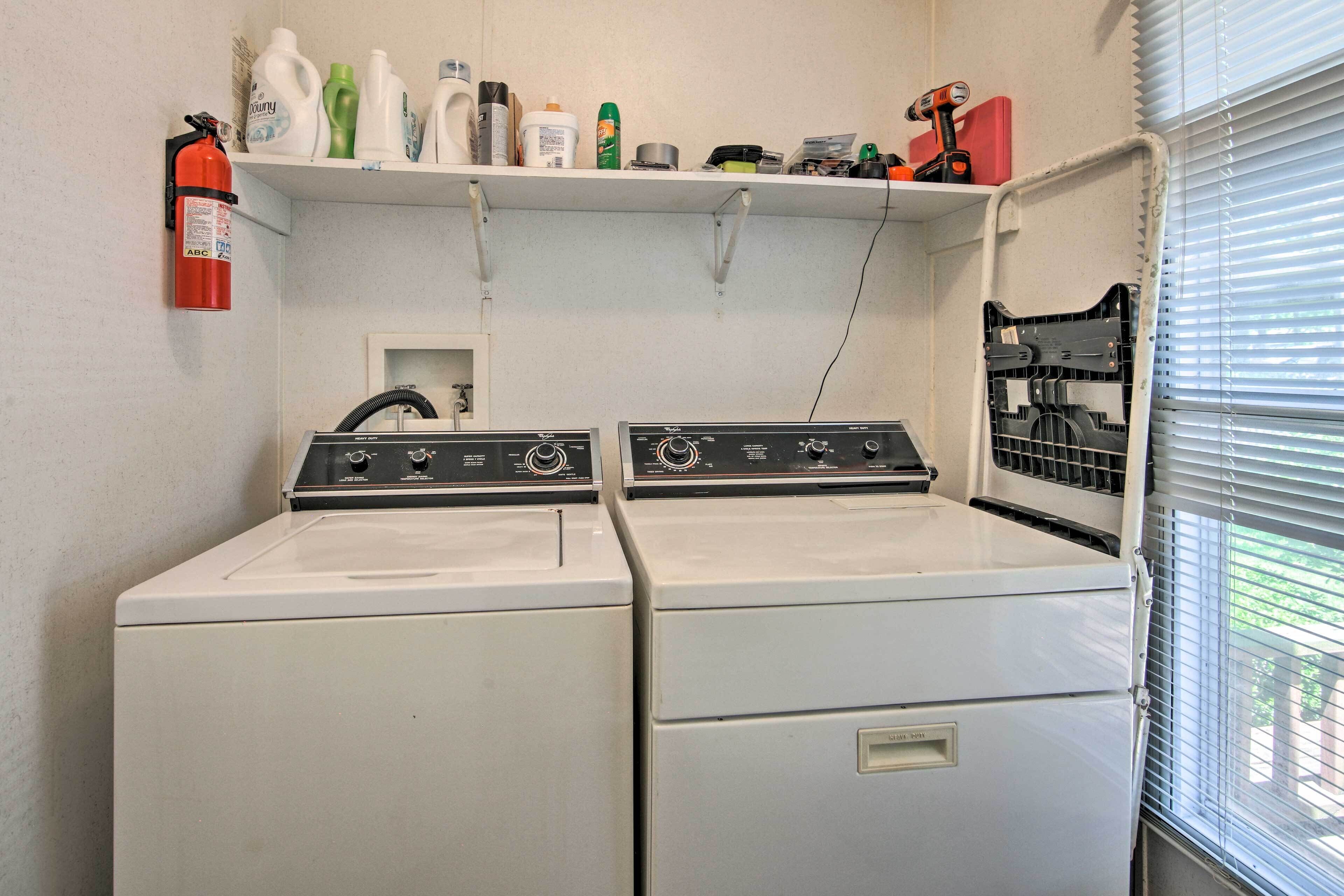 A laundry room with two stacked washers and dryers, a fire extinguisher, and a shelf with cleaning supplies.