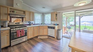 A modern kitchen with wooden cabinets, stainless steel appliances, and a large window overlooking a backyard.