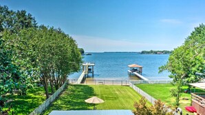 A view of a lake with a dock, a grassy area, and a building with a roof.