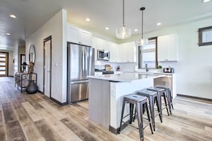 A modern kitchen with white cabinets, stainless steel appliances, and a central island with bar stools. - Modern Bozeman Family Townhome w/ Hot Tub! (Bozeman)