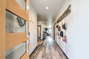 A hallway with wooden flooring, a glass door on the left, and a wall with hats hanging on the right. - Modern Bozeman Family Townhome w/ Hot Tub! (Bozeman)