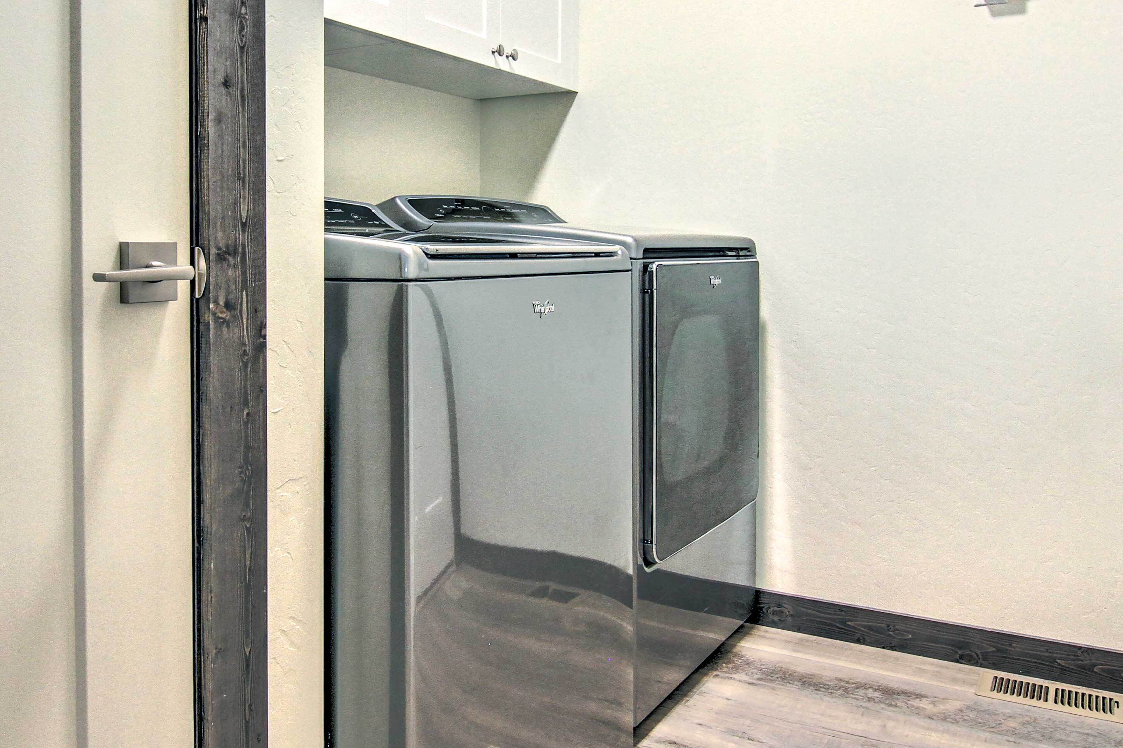 A laundry room with two front-loading washers and dryers, a wooden door, and a white wall.