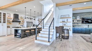 A modern kitchen with a central island, wooden beams, and a staircase.