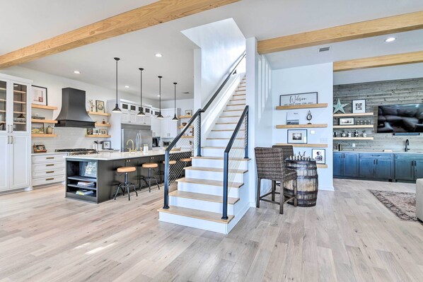 A modern kitchen with a central island, wooden beams, and a staircase. - Entire Luxury Lake Granbury Cliffside Home w/ Deck (Granbury)