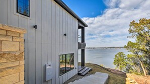 A modern house with a stone foundation, a large window, and a view of a lake. - Entire Luxury Lake Granbury Cliffside Home w/ Deck (Granbury)