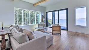 A spacious living room with a large window, a wooden ceiling, and a view of the sea.