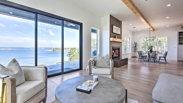 A spacious living room with large windows, a fireplace, and a dining area with a view of the sea.