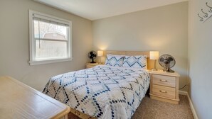 Ein Schlafzimmer mit einem Bett, Nachttischen, einem Schreibtisch, einem Fenster und einer Deckenleuchte.