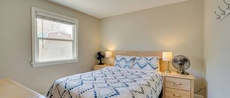 A bedroom with a bed, bedside tables, a desk, a window, and a ceiling light.