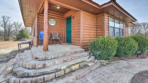 A log cabin with a porch, a green door, and a small outdoor seating area. - Pet-friendly Cabin Rental Retreat! (Keota)
