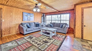 A cozy living room with wooden walls, two grey sofas, a coffee table, and a patterned rug. - Pet-friendly Cabin Rental Retreat! (Keota)