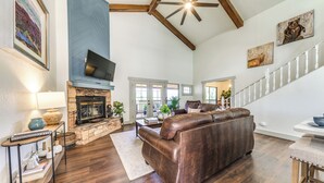 A spacious living room with a fireplace, leather sofa, and a staircase leading to another level. - 'moondance' Ruidoso Retreat w/ Hot Tub & Views! (Ruidoso)