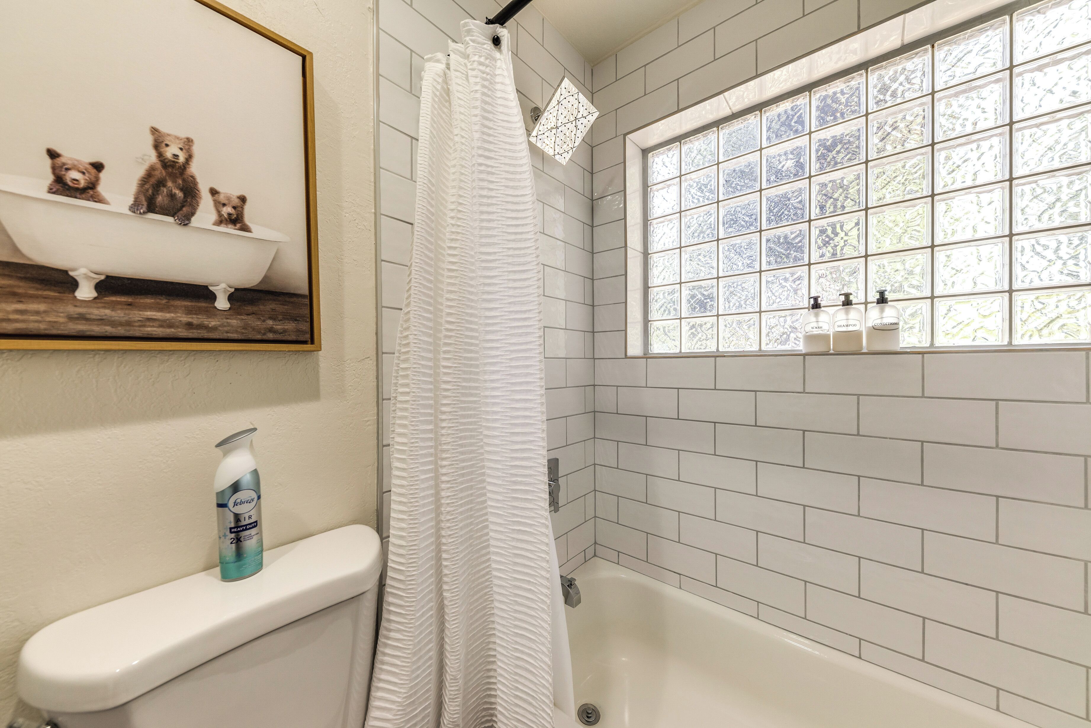 A bathroom with a bathtub, a toilet, a window with a view, and a shelf with decorative items.