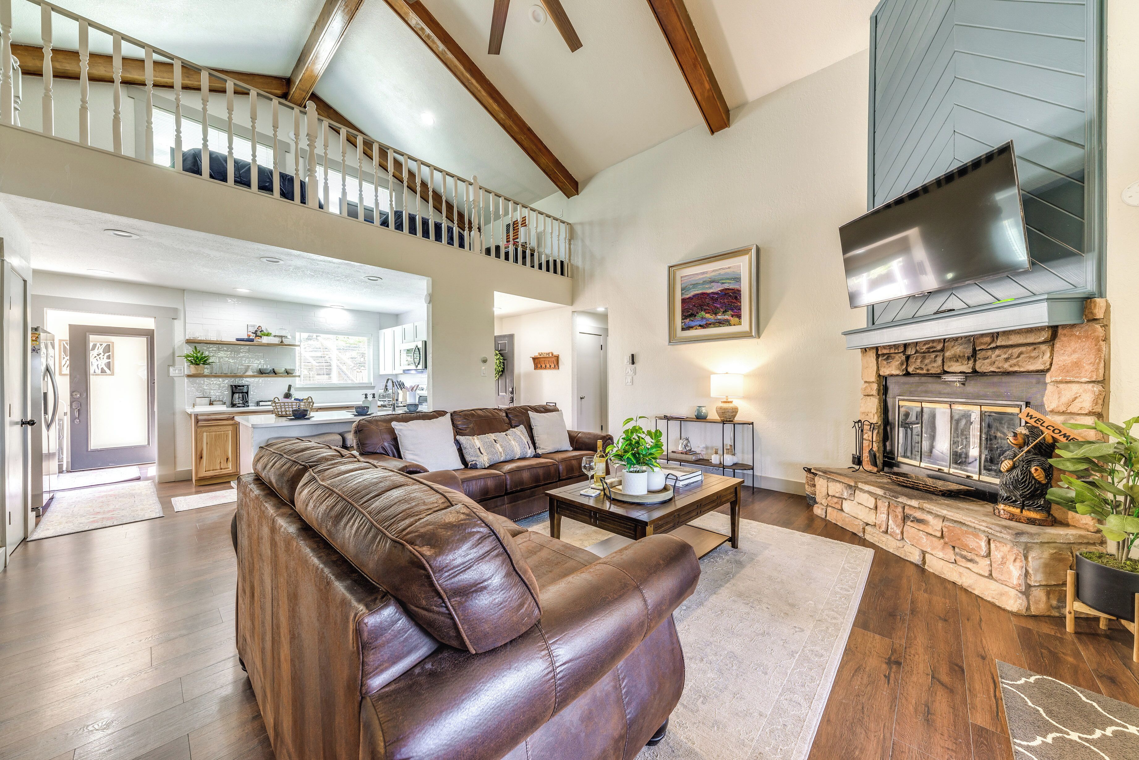 A spacious living area with a brown leather sofa, a stone fireplace, and a kitchen in the background.