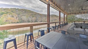 An outdoor patio with tables and chairs, overlooking a river and forested hills. - Lavish Riverfront Escape w/ Gas Grill! (Glenwood)