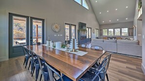 A spacious dining area with a long wooden table and chairs, large windows, and a high ceiling with recessed lighting. - Lavish Riverfront Escape w/ Gas Grill! (Glenwood)