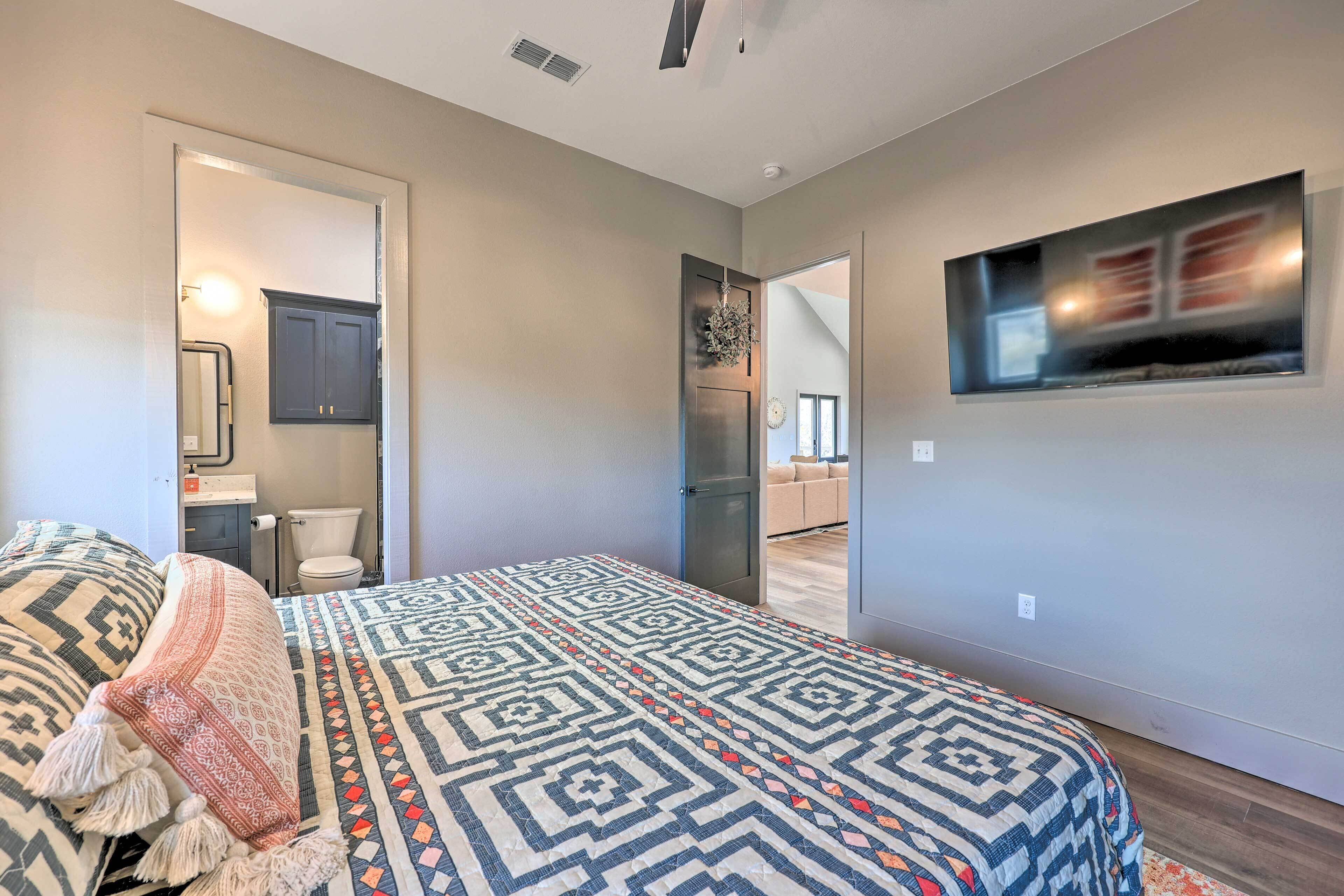 A bedroom with a patterned bedspread, a large window, and a flat-screen TV mounted on the wall.