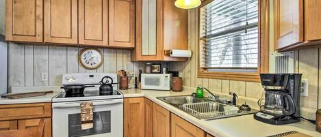 A kitchen with wooden cabinets, a stove, a microwave, a coffee maker, and a window with blinds.