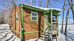 A wooden cabin with a green door and windows, a covered porch, and a staircase leading up to the entrance. - Secluded Remer Cabin w/ Lake Access! (Remer)