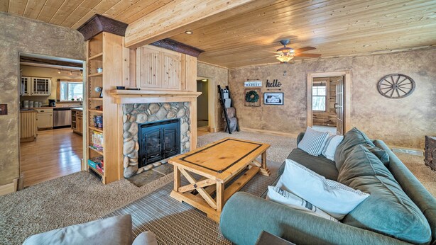 A cozy living room with a stone fireplace, wooden ceiling, and a large sofa. - 'the Farmstead' on 10 Acres w/ Mountain Views! (Red Lodge)
