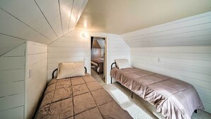 A small, cozy room with two beds, a sloped ceiling, and a doorway leading to another room. - 'the Farmstead' on 10 Acres w/ Mountain Views! (Red Lodge)