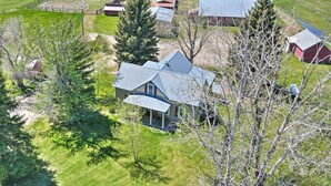 An aerial view of a rural property with multiple buildings, including a large house with a porch and a fenced area. - 'the Farmstead' on 10 Acres w/ Mountain Views! (Red Lodge)