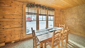 A wooden cabin interior with a dining table set for four, large windows, and a view of a snowy landscape. - 'the Farmstead' on 10 Acres w/ Mountain Views! (Red Lodge)