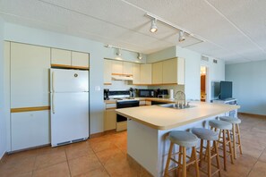 A kitchen with a central island, bar stools, a refrigerator, microwave, oven, and a television.