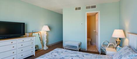 A bedroom with a bed, a dresser, a television, a lamp, and a door leading to a bathroom.
