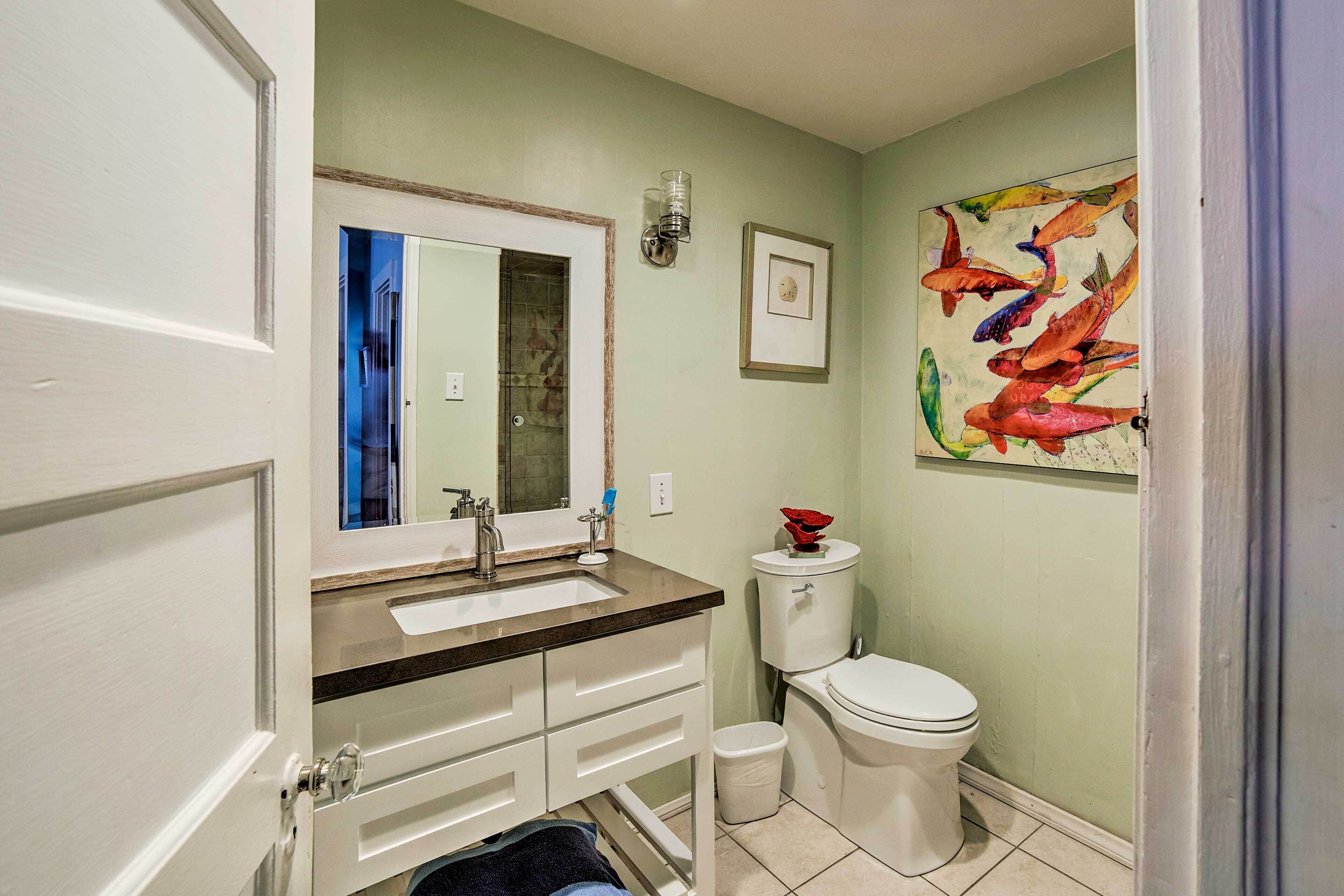 A bathroom with a white toilet, a sink with a mirror, and a trash can.