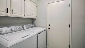 A laundry room with a front-loading washer and dryer, white cabinets, and a door. - Stunning Plano Home w/ Private Pool & Hot Tub (Plano)