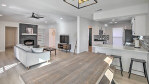 A modern living room with a fireplace, a sofa, a dining table, and a kitchen area with a bar. - Stunning Plano Home w/ Private Pool & Hot Tub (Plano)