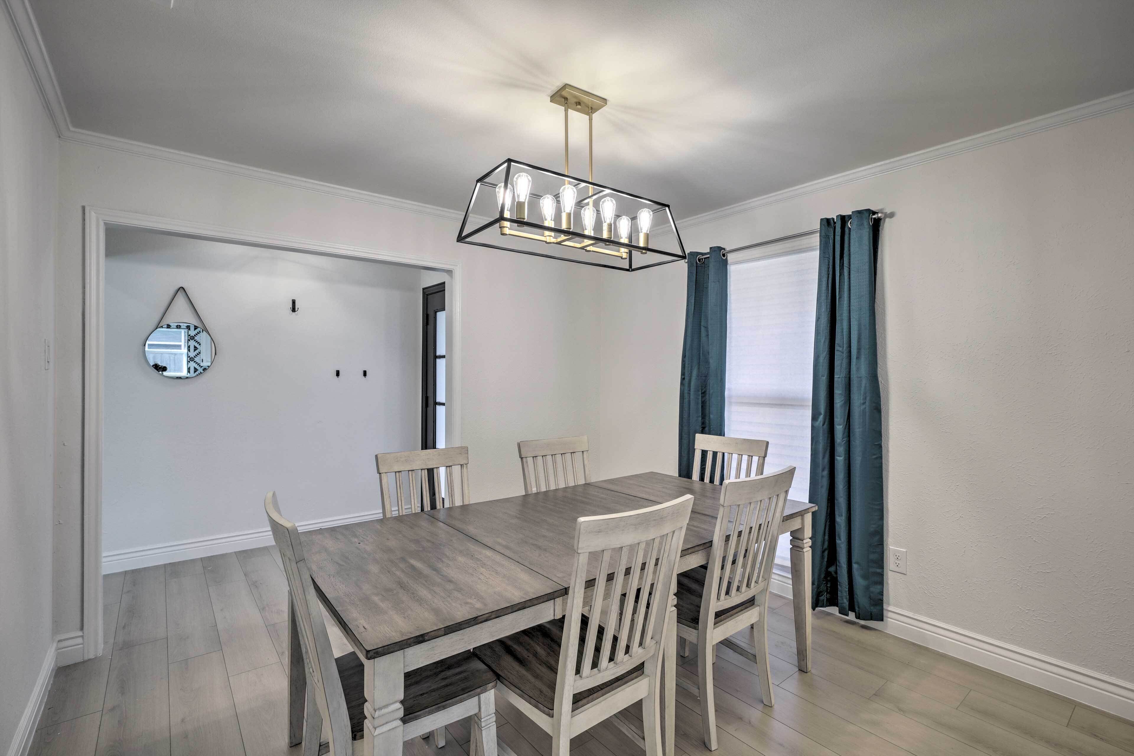 Un coin repas comprenant une table rectangulaire et six chaises, un lustre et un miroir au mur.