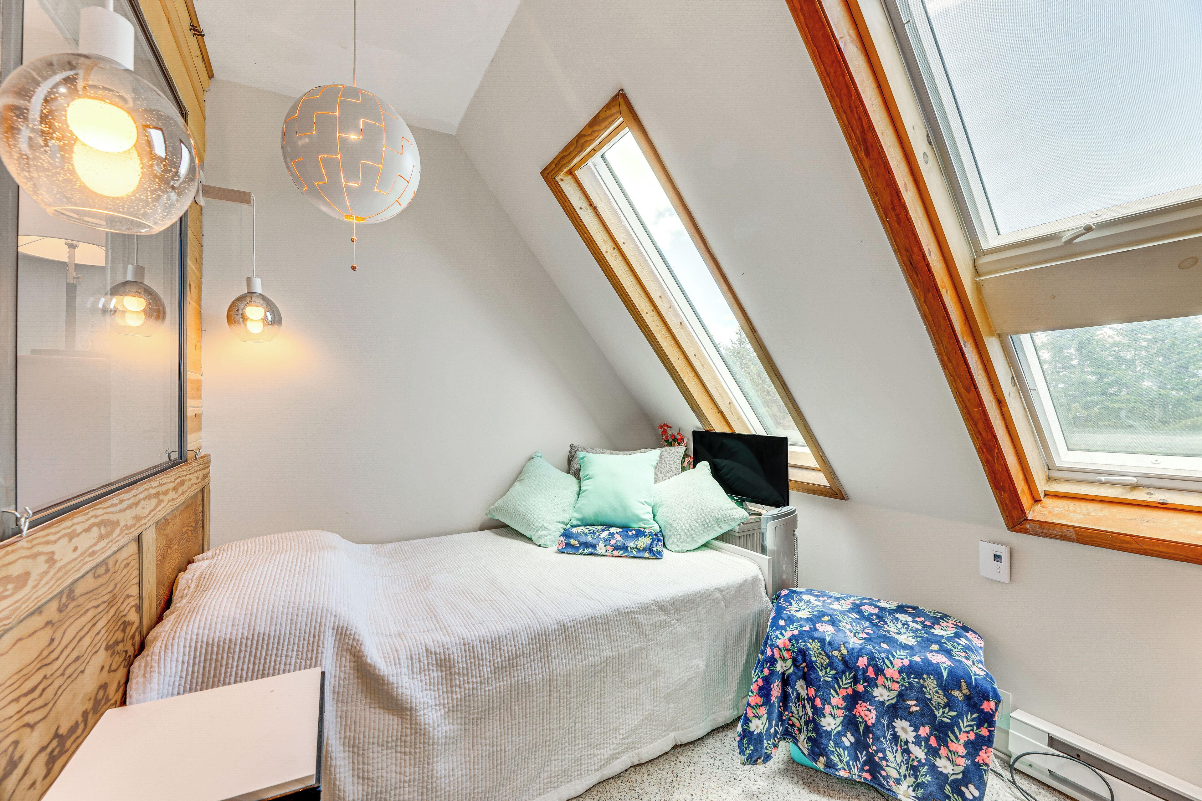 A bedroom with a sloped ceiling, a bed with a white and blue floral bedspread, a small table with a blue floral tablecloth, and a TV on a stand.
