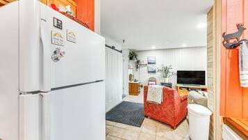 Eine kompakte Küche mit Kühlschrank, ein Essbereich mit Tisch und Stühlen, ein Fernseher und ein rotes Sofa.