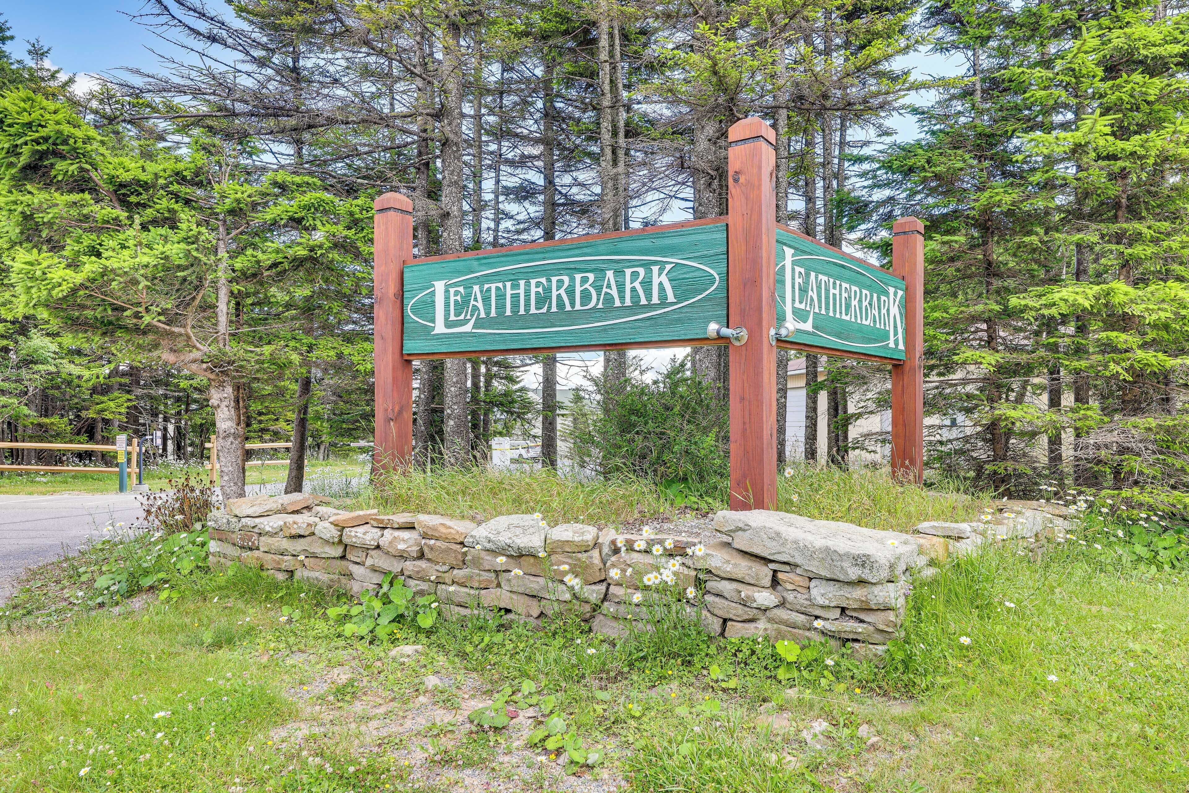 A sign for Leatherbark with a stone wall and greenery around.